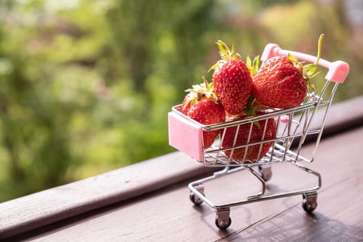 Little shopping cart filled with raw delicious strawberries. Concept shot symbolizing buying healthy food or ordering online