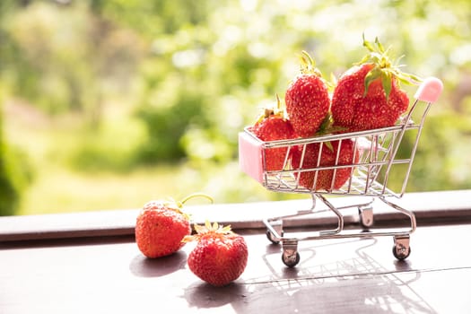 Little shopping cart filled with raw delicious strawberries. Concept shot symbolizing buying healthy food or ordering online