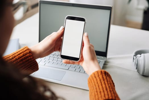 Over shoulder view of woman holding mobile phone with white blank mock up cellular screen applications working using cell phone. Cellphone display mock up for advertising apps concept