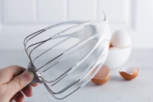 Whisked egg whites - whipped Italian meringue on a wire whisk and eggs on a gray background. copy space.