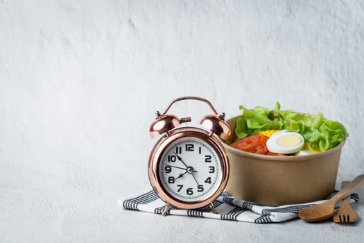 Fresh healthy salad with an alarm clock for the concept of food, time management, diet and heathy eating concept