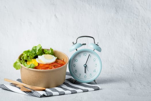 Fresh healthy salad with an alarm clock for the concept of food, time management, diet and heathy eating concept