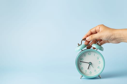 The bell alarm clock is turned off by hand against blue background for the concept of time management.