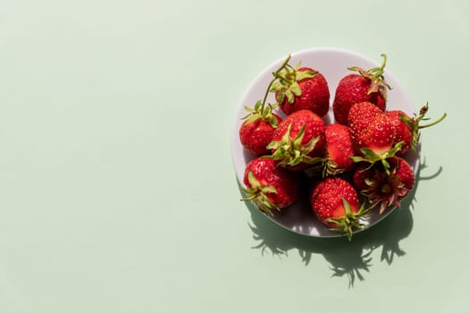 Heap of fresh strawberries in ceramic bowl on rustic white wooden background.