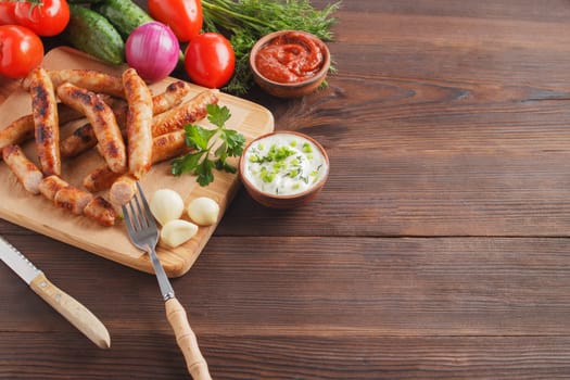 Delicious sausages on a wooden board with various sauces and fresh vegetables on a wooden table. copy space.