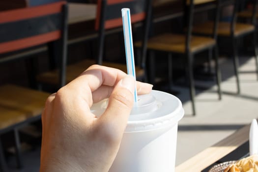 White plastic cup and straw in hand close up