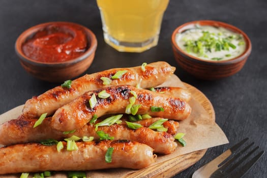 Tasty sausages on a wooden board with various sauces with a glass of beer on a black background.