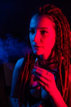 Caucasian girl with dreadlocks smokes a vape in red blue light