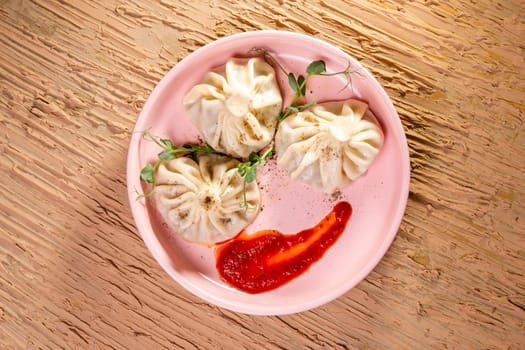 top view of three khinkali with red sauce on a pink plate.