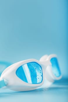 White swimming glasses with a blue lens on a blue background