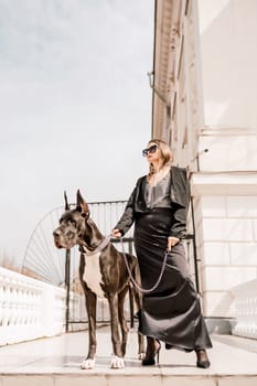 A woman walks with her Great Dane in an urban setting, enjoying the outdoors and the company of her dog