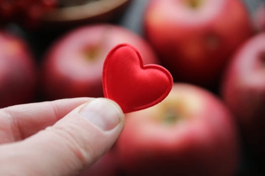 Hand holding a heart on the background of an apple healthy food idea.