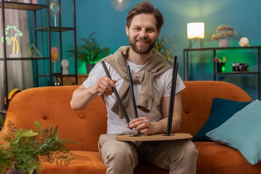 Happy man finishing assembling furniture at home. Successful table desk collect, repair, fixing. Caucasian guy after moving into new apartment. Advertisement of a furniture store. Mortgage, lifestyle