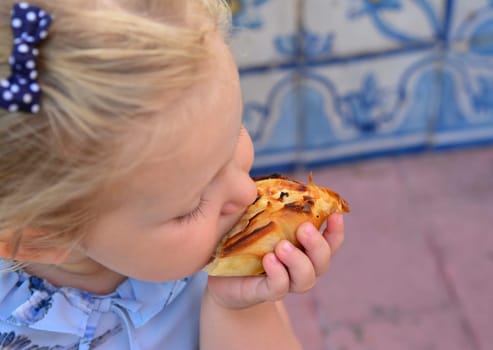 The girl is eating Pasteis de Belem egg tart. Azulejos tile on a background