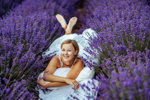 A middle-aged woman lies in a lavender field and enjoys aromatherapy. Aromatherapy concept, lavender oil, photo session in lavender.