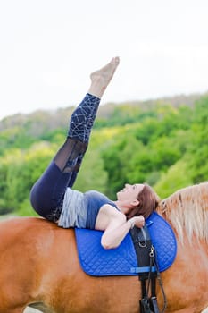 young woman doing yoga on a horse against the backdrop of trees.