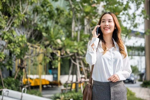 Happy businesswoman working talking on smartphone outdoor in city with client, Asian business female calling on smart mobile phone and walking on street outside office building, business communication