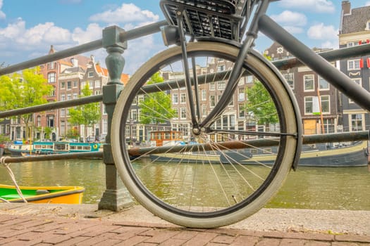 Netherlands. Summer day in Amsterdam. View through a bicycle wheel to the canal embankment with authentic land-based houses and houseboats near the shore