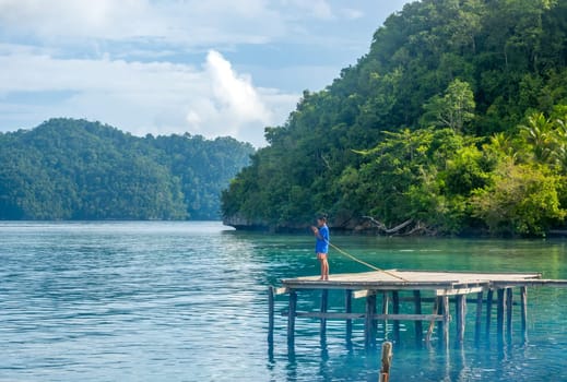 Indonesia. Rustic pier on one of the thousands of tropical islands. The boy puts the bait on the hook of his fishing rod