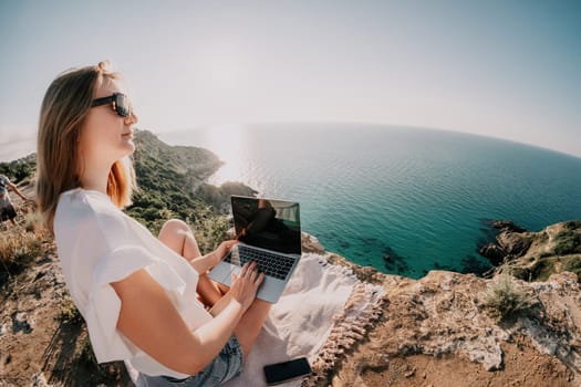 Woman sea laptop. Business woman in yellow hat working on laptop by sea. Close up on hands of pretty lady typing on computer outdoors summer day. Freelance, digital nomad, travel and holidays concept.