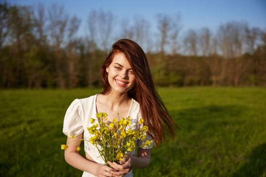 Beautiful woman in a white dress with a bouquet of yellow wildflowers walking in a field . High quality photo