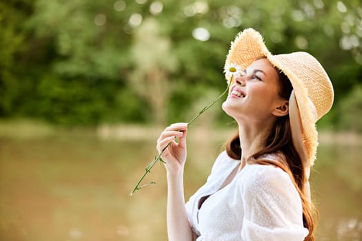 close-up portrait of a happy woman in a wicker hat with a camomile in her hands on the background of the lake. High quality photo