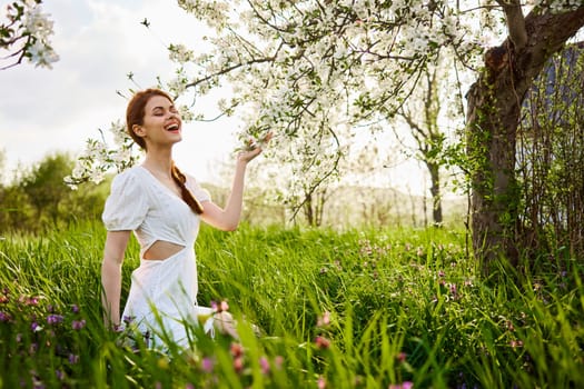 a woman in a light dress sits in the grass near a flowering apple tree. High quality photo