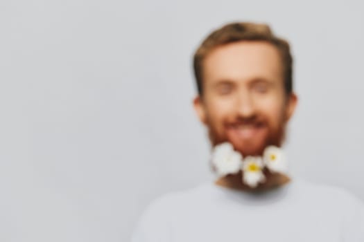 Portrait of a funny man in a white T-shirt with flowers daisies in his beard on a white isolated background, copy place. Holiday concept and congratulations. High quality photo