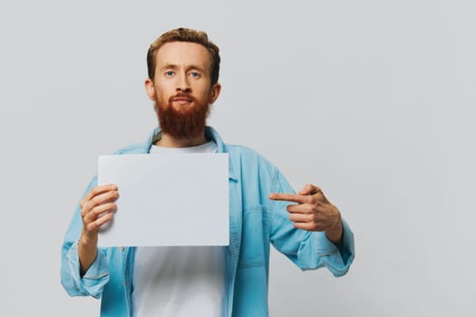 Portrait of an adult male on a gray background with a white sheet of paper in his hands for your design and text, layout, copy space, space for text, finger pointing. High quality photo