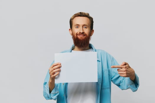Portrait of an adult male on a gray background with a white sheet of paper in his hands for your design and text, layout, copy space, space for text, finger pointing. High quality photo