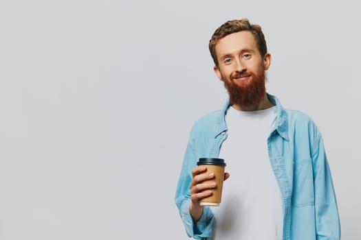 Man hipster with a cup of coffee with a smile on a gray background in a blue shirt and white t-shirt. High quality photo