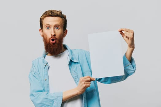 Portrait of an adult male on a gray background with a white sheet of paper in his hands for your design and text, layout, copy space, space for text, finger pointing. High quality photo