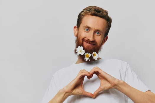 Portrait of a funny man in a white T-shirt with flowers daisies in his beard on a white isolated background, copy place. Holiday concept and congratulations. High quality photo