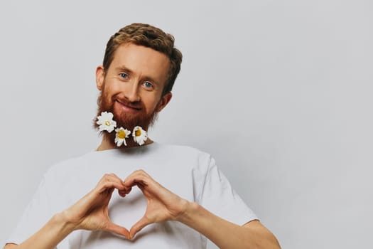 Portrait of a funny man in a white T-shirt with flowers daisies in his beard on a white isolated background, copy place. Holiday concept and congratulations. High quality photo