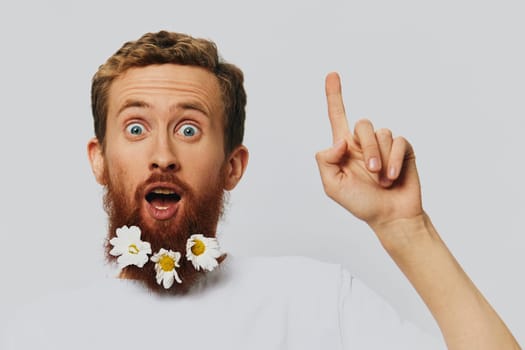 Portrait of a funny man in a white T-shirt with flowers daisies in his beard on a white isolated background, copy place. Holiday concept and congratulations. High quality photo