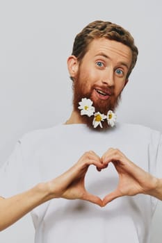 Portrait of a funny man in a white T-shirt with flowers daisies in his beard on a white isolated background, copy place. Holiday concept and congratulations. High quality photo