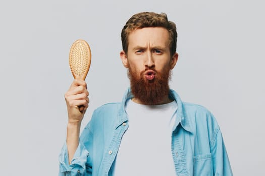Portrait of a man with a massage comb in his hands, combing his hair and beard, hair loss problem. High quality photo