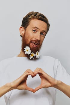 Portrait of a funny man in a white T-shirt with flowers daisies in his beard on a white isolated background, copy place. Holiday concept and congratulations. High quality photo