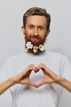 Portrait of a funny man in a white T-shirt with flowers daisies in his beard on a white isolated background, copy place. Holiday concept and congratulations. High quality photo