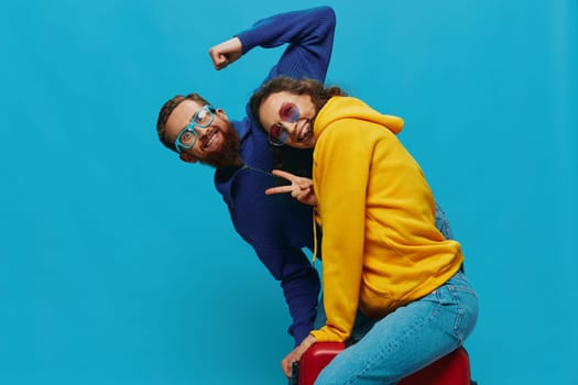 Woman and man smile sitting on suitcase with red suitcase smile, on blue background, packing for trip, family vacation trip. High quality photo