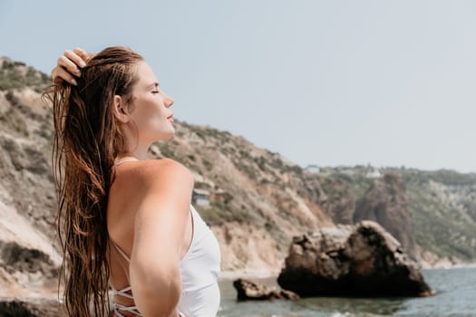 Woman travel sea. Young Happy woman in a long red dress posing on a beach near the sea on background of volcanic rocks, like in Iceland, sharing travel adventure journey