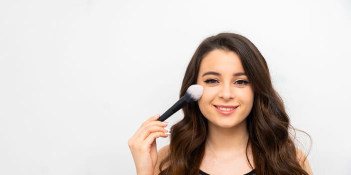 Portrait of cheerful laughing woman applying powder on her cheek with a brush. Skincare and cosmetic procedures.