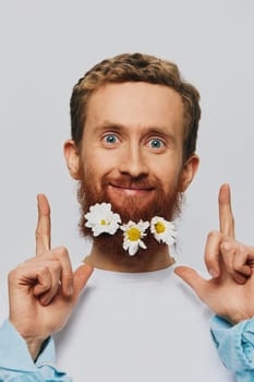 Portrait of a funny man in a white T-shirt with flowers daisies in his beard on a white isolated background, copy place. Holiday concept and congratulations. High quality photo