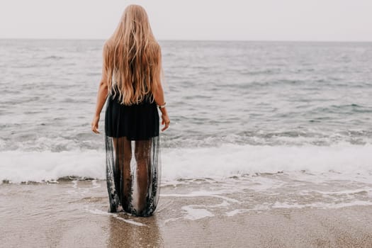 Woman travel sea. Young Happy woman in a long red dress posing on a beach near the sea on background of volcanic rocks, like in Iceland, sharing travel adventure journey