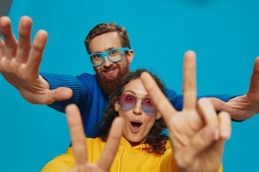 A woman and a man fun couple cranking and showing signs with their hands smiling cheerfully, on a blue background, The concept of a real relationship in a family. High quality photo