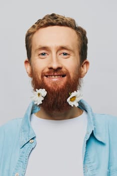 Portrait of a funny man in a white T-shirt with flowers daisies in his beard on a white isolated background, copy place. Holiday concept and congratulations. High quality photo