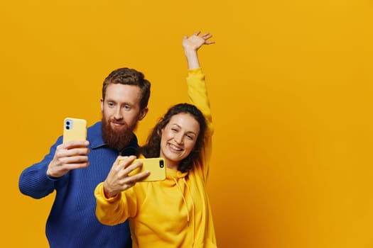 Man and woman couple smiling merrily with phone in hand social media viewing photos and videos, on yellow background, symbols signs and hand gestures, family freelancers. High quality photo