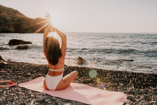 Young woman in swimsuit with long hair practicing stretching outdoors on yoga mat by the sea on a sunny day. Women's yoga fitness pilates routine. Healthy lifestyle, harmony and meditation concept.