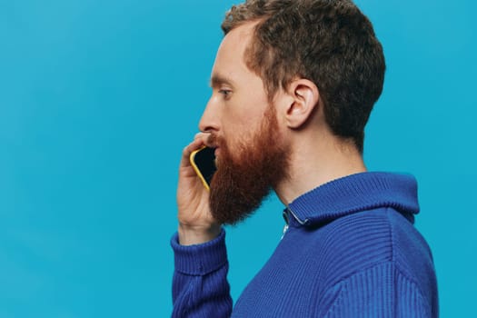 Portrait of a man with a phone in his hands does looking at it and talking on the phone, on a blue background. Communicating online social media, lifestyle. High quality photo