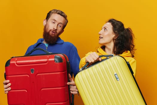 Woman and man smiling, suitcases in hand with yellow and red suitcase smiling merrily and crooked, yellow background, going on a trip, family vacation trip, newlyweds. High quality photo